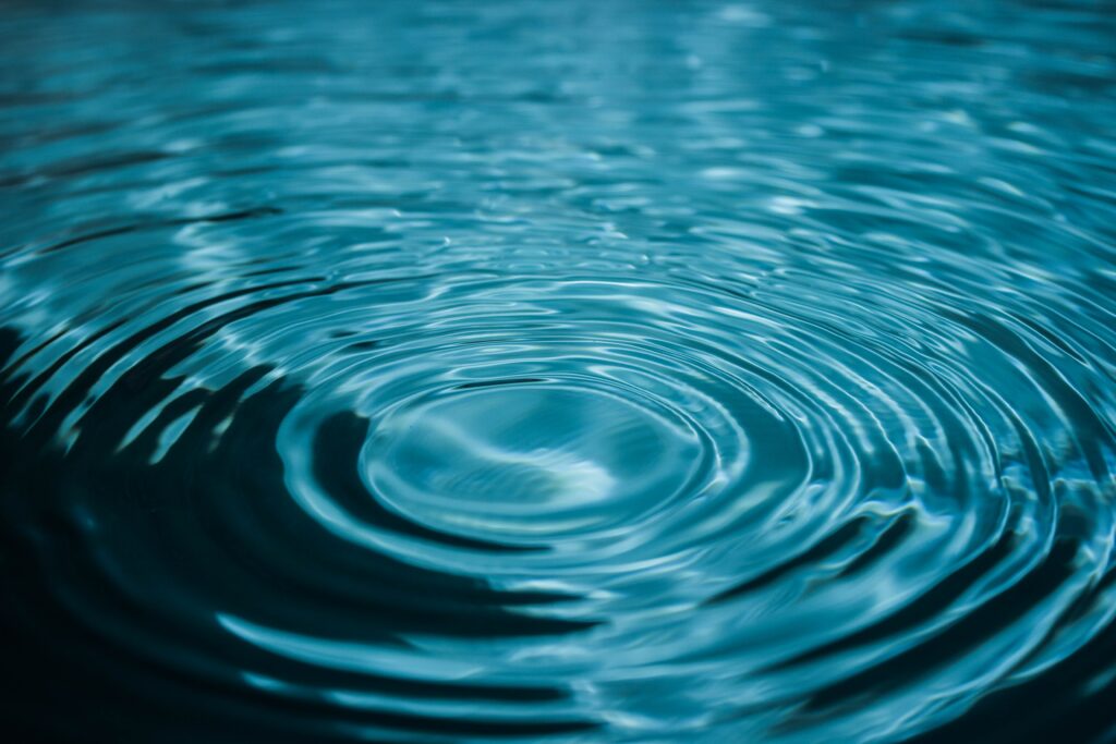 “Serene Close-Up: Ripples Creating Circles on Calm Blue Water Wallpaper”