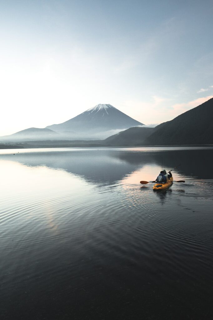 Person paddling yellow canoe on calm sea with volcano and mountains under morning sky wallpaper