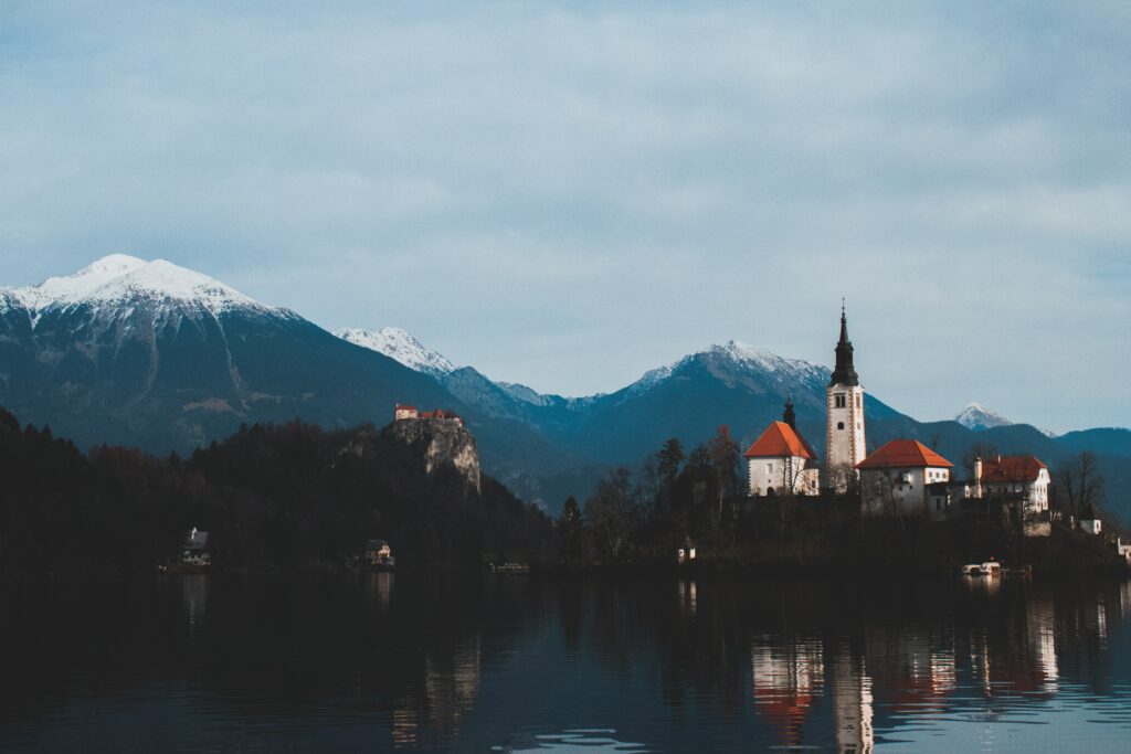 Serene castle and tall tower reflected on calm lake with snow-capped mountains background wallpaper