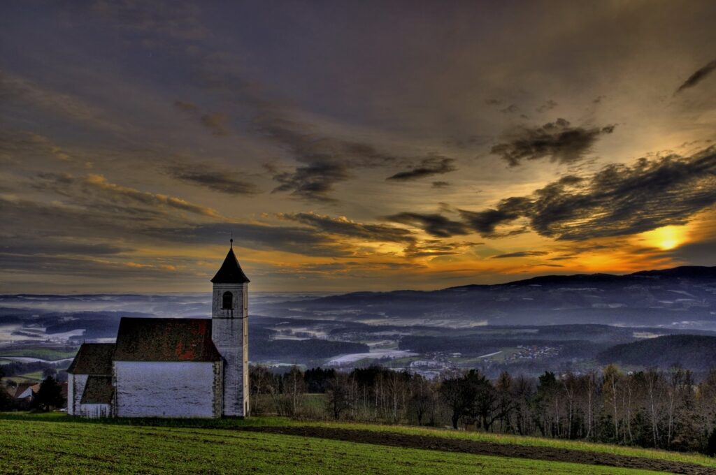 Serene chapel overlooking misty mountains under golden sunrise sky with swirling clouds wallpaper