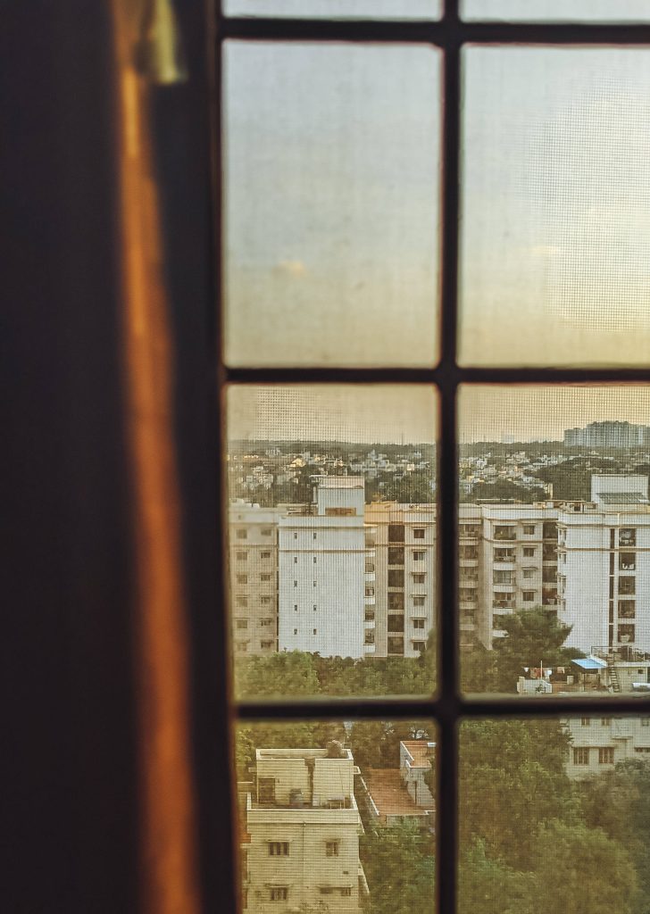 Golden hour cityscape through grid window with buildings and trees calm HD wallpaper background
