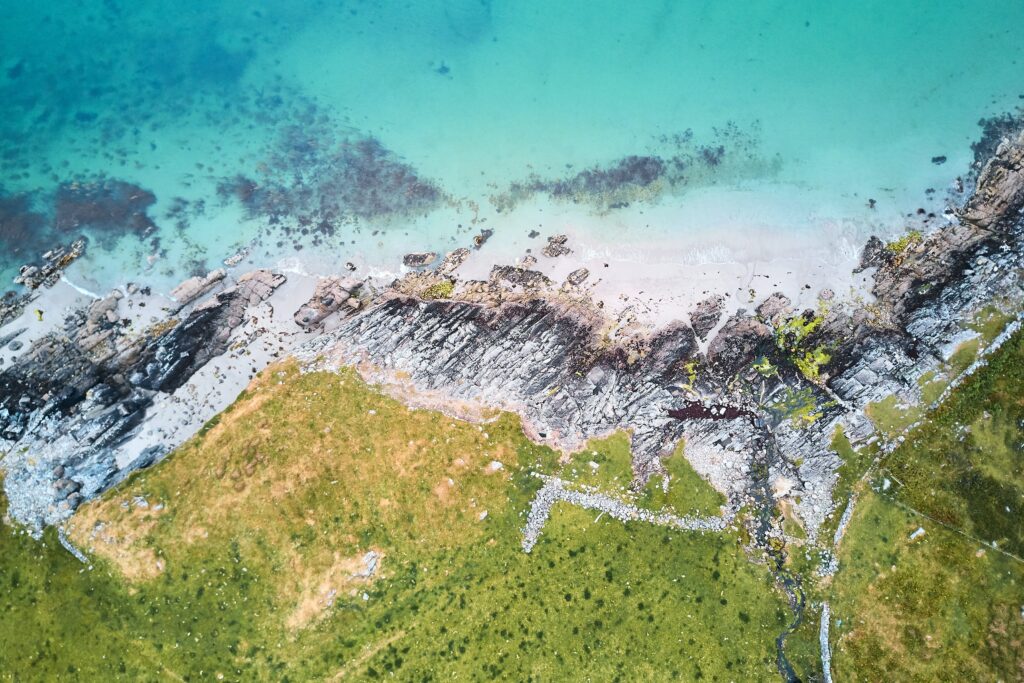 Aerial view of rugged rocks turquoise sea and lush green grass along serene coastal shoreline wallpaper