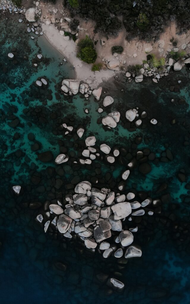 Aerial view of serene coastal shoreline with scattered stones turquoise water and lush greenery Wallpaper