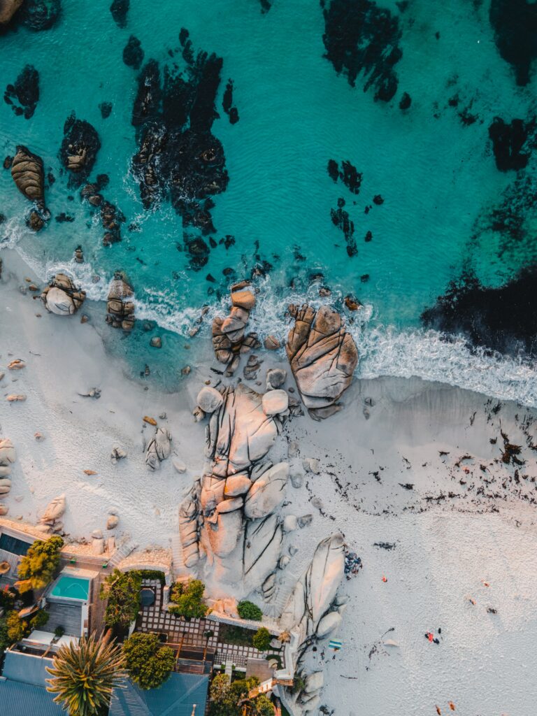 Aerial view of turquoise sea sandy beach rocks palm trees and modern buildings coastal scene wallpaper