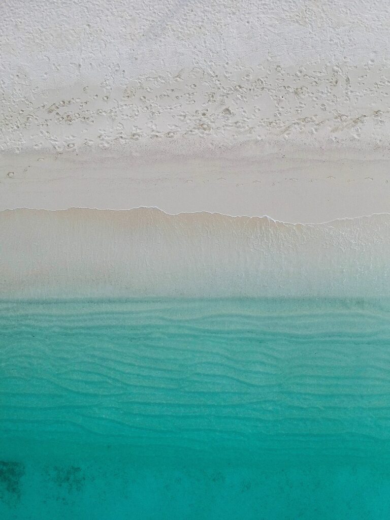 Aerial view of turquoise ocean waves gently meeting soft white sandy beach serene seascape wallpaper