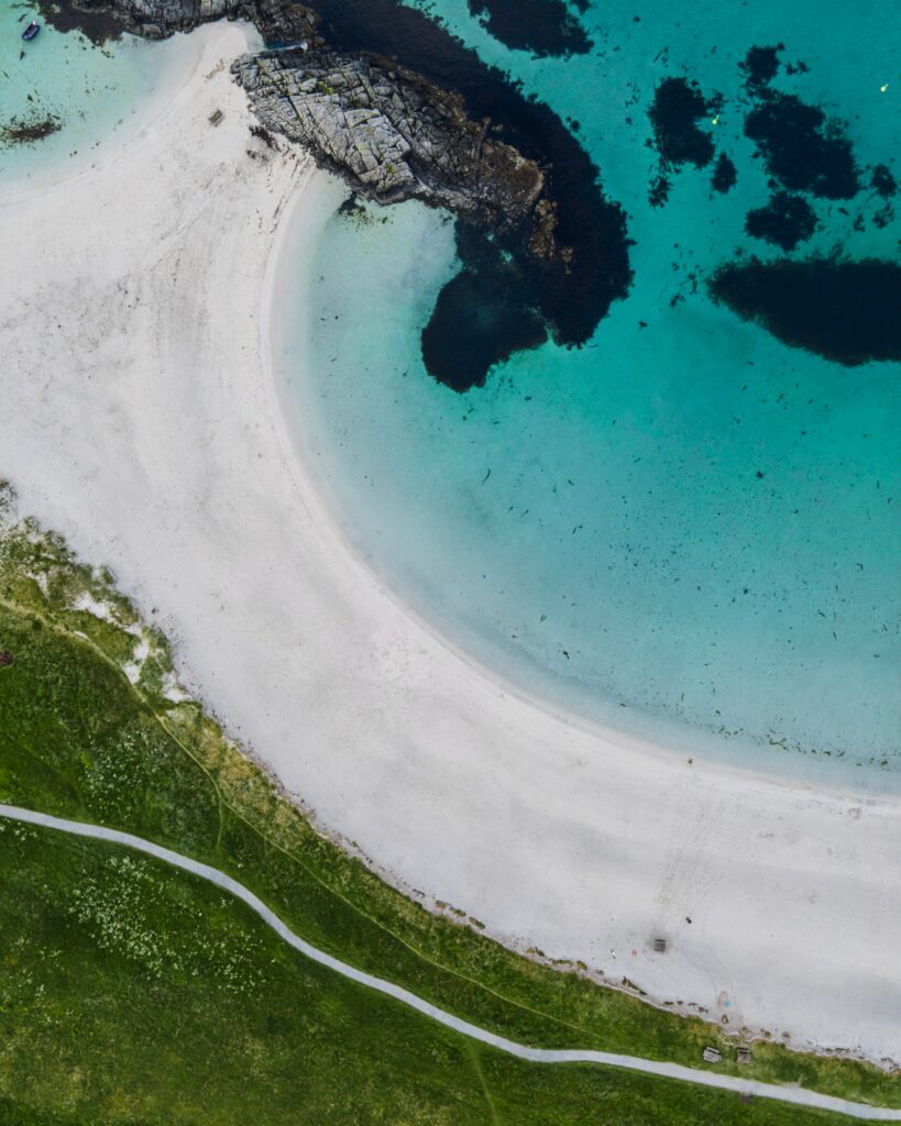 Aerial view of serene coastline with white sand turquoise water rugged rocks and green grass Wallpaper