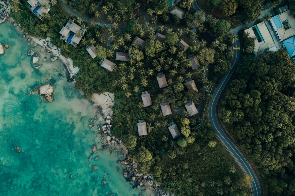 Aerial view of turquoise sea coastal landscape with lush greenery winding road and buildings Wallpaper