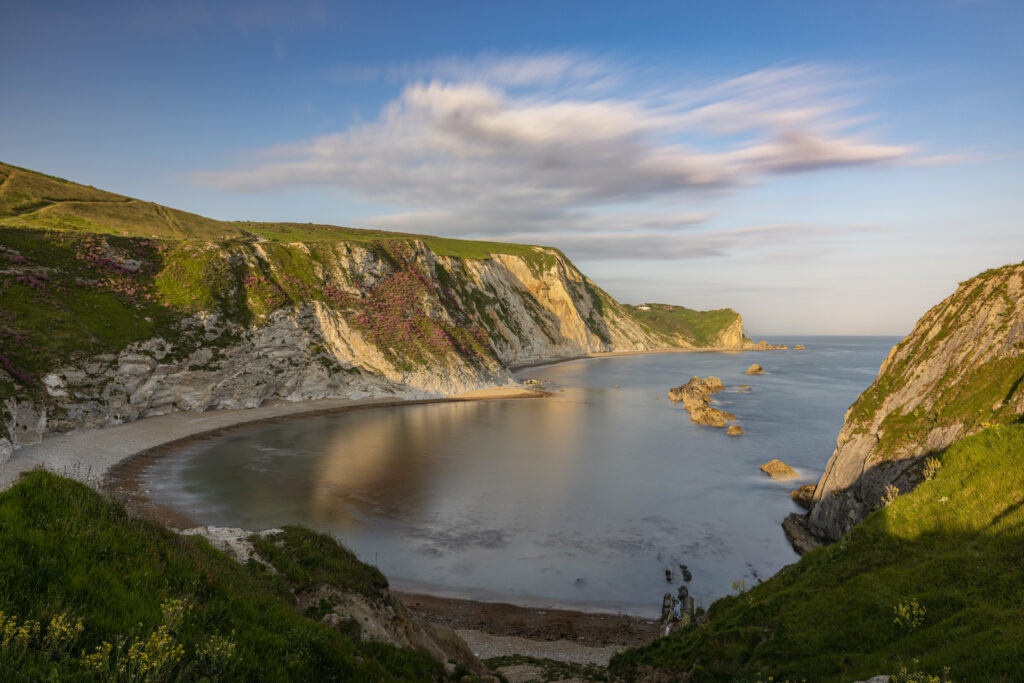 Serene coastal bay with rugged rocks lush green cliffs calm sea reflecting golden sunset light wallpaper