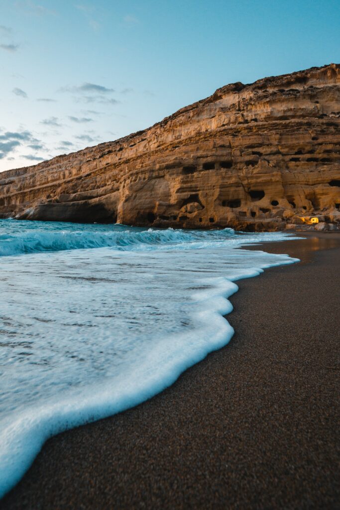 Serene coastal wallpaper with gentle waves soft sand rugged rocks golden lit cliff clear blue sky