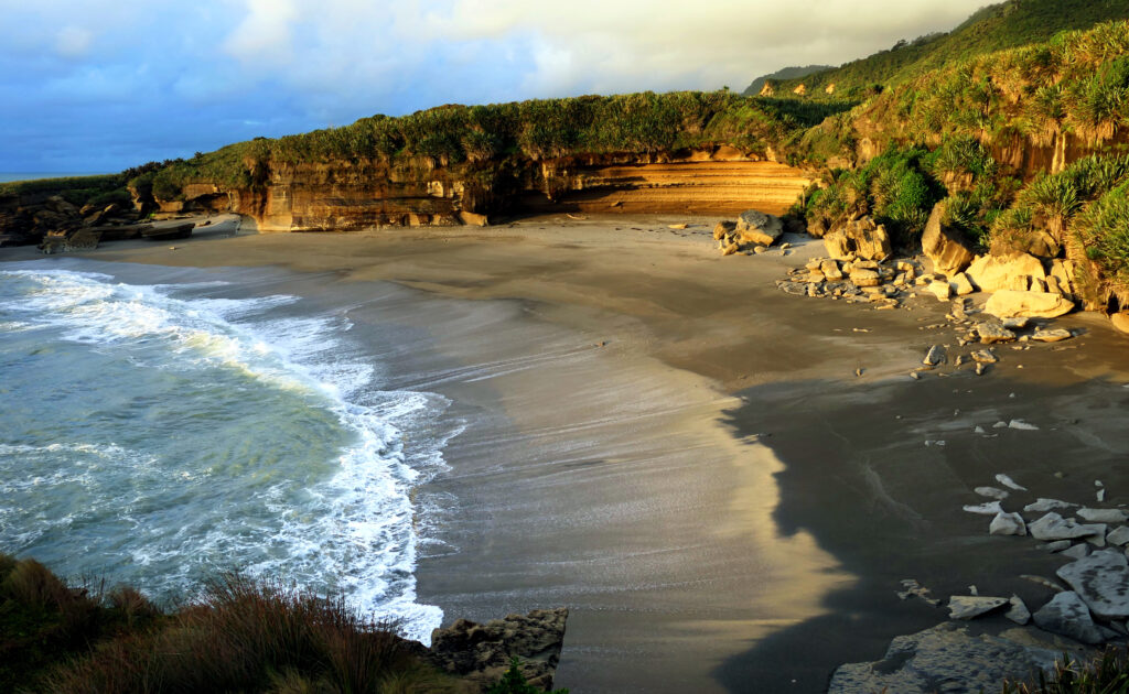 Serene coastal wallpaper with gentle waves sandy shore rocky formations and lush greenery landscape