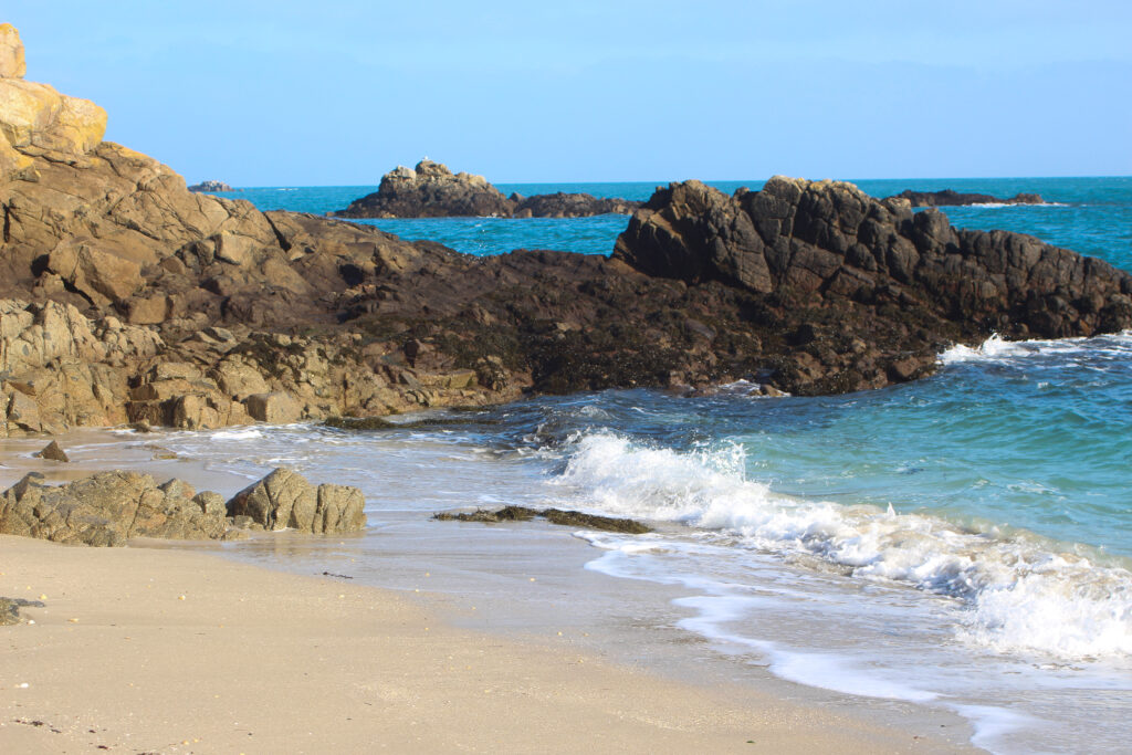 Serene coastal wallpaper with rugged rocks turquoise sea gentle waves sandy beach clear skies