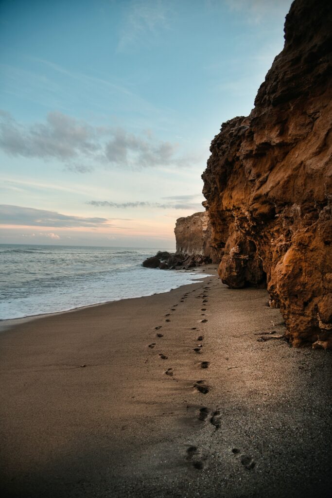 Serene coastal scene with rugged rocks sandy beach gentle waves and footprints in wet sand wallpaper