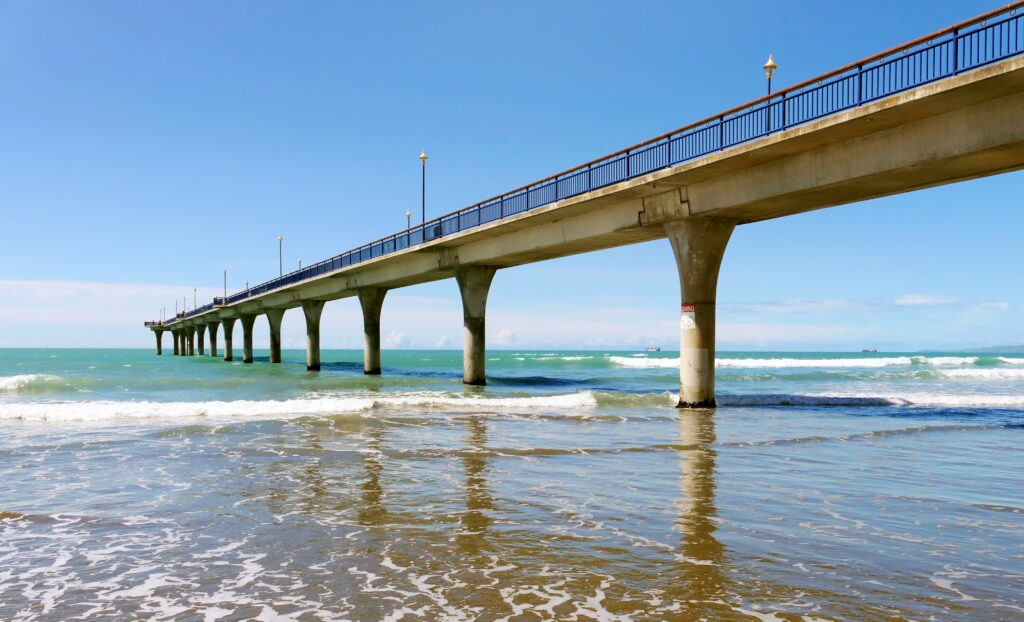 Long bridge over vibrant blue sea with sandy shore and gentle waves under bright sky wallpaper