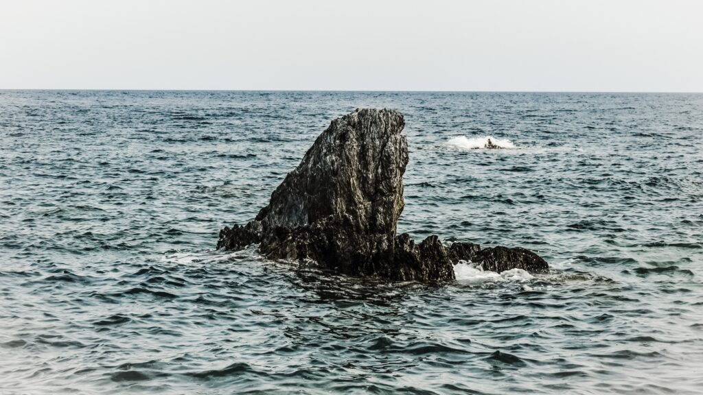 Rugged cliff over deep blue choppy sea under pale overcast sky serene coastal scene wallpaper