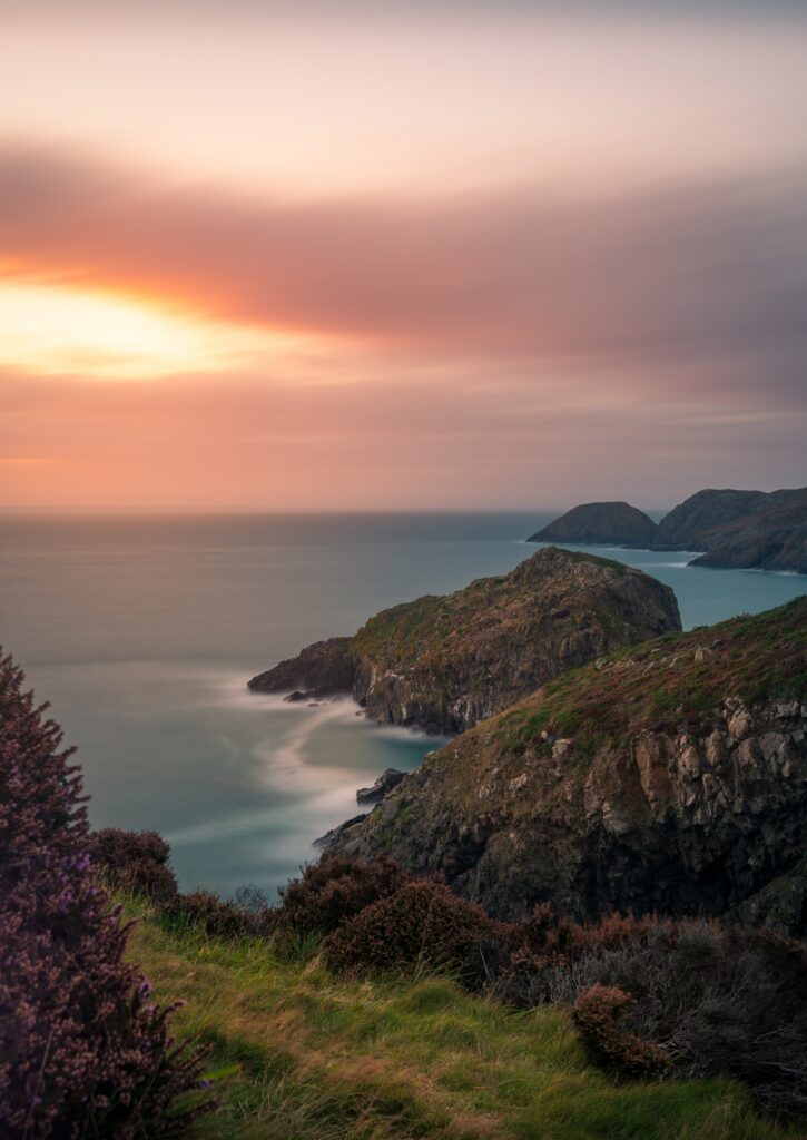 Coastal cliff with rugged rocks rolling grass serene sea colorful sunset sky natural landscape wallpaper