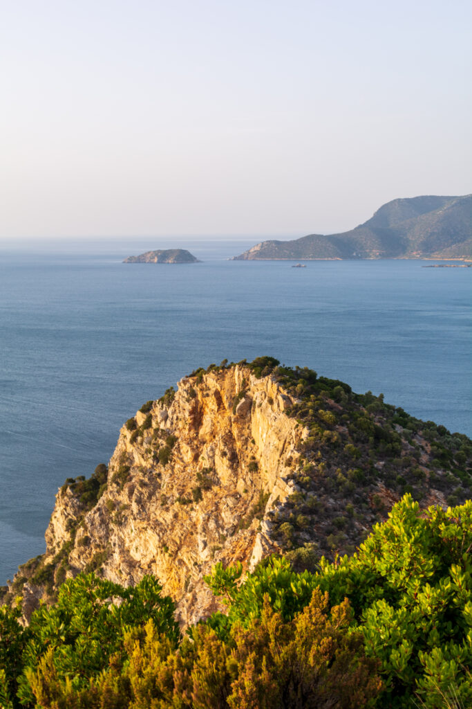 Aerial view of rugged rocks green trees calm sea distant islands mountains serene coastal landscape Wallpaper