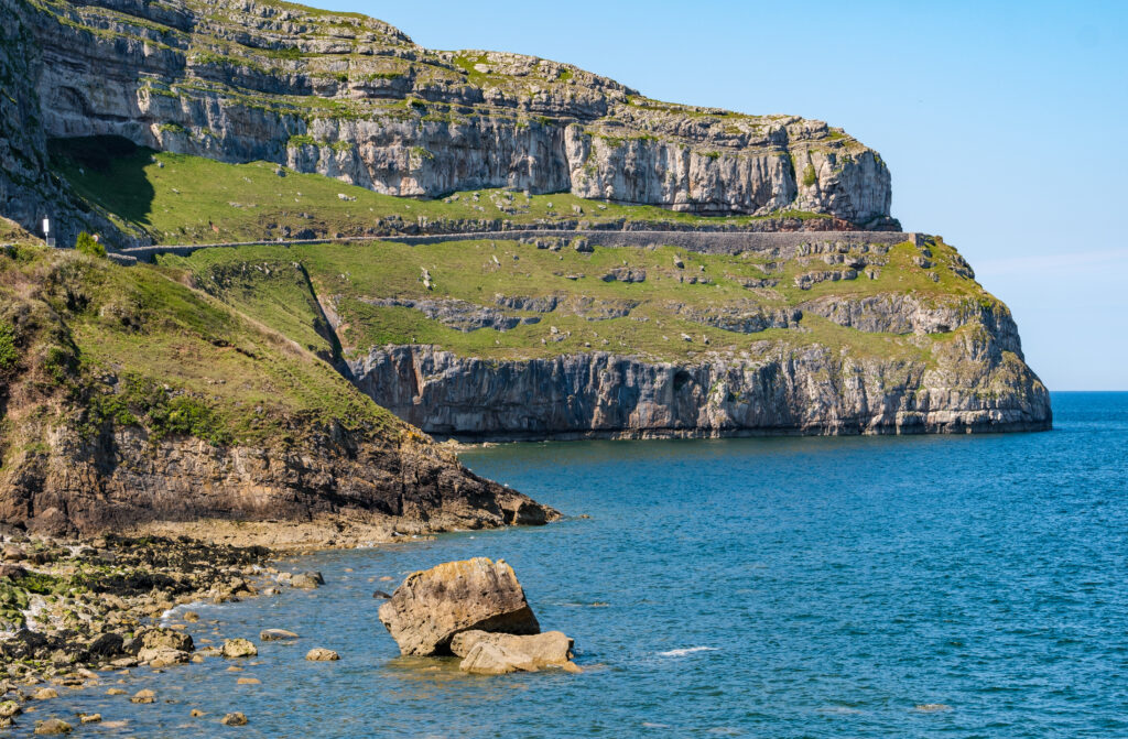Stunning coastal cliffs with weathered rocks and calm blue sea under clear sky wallpaper background