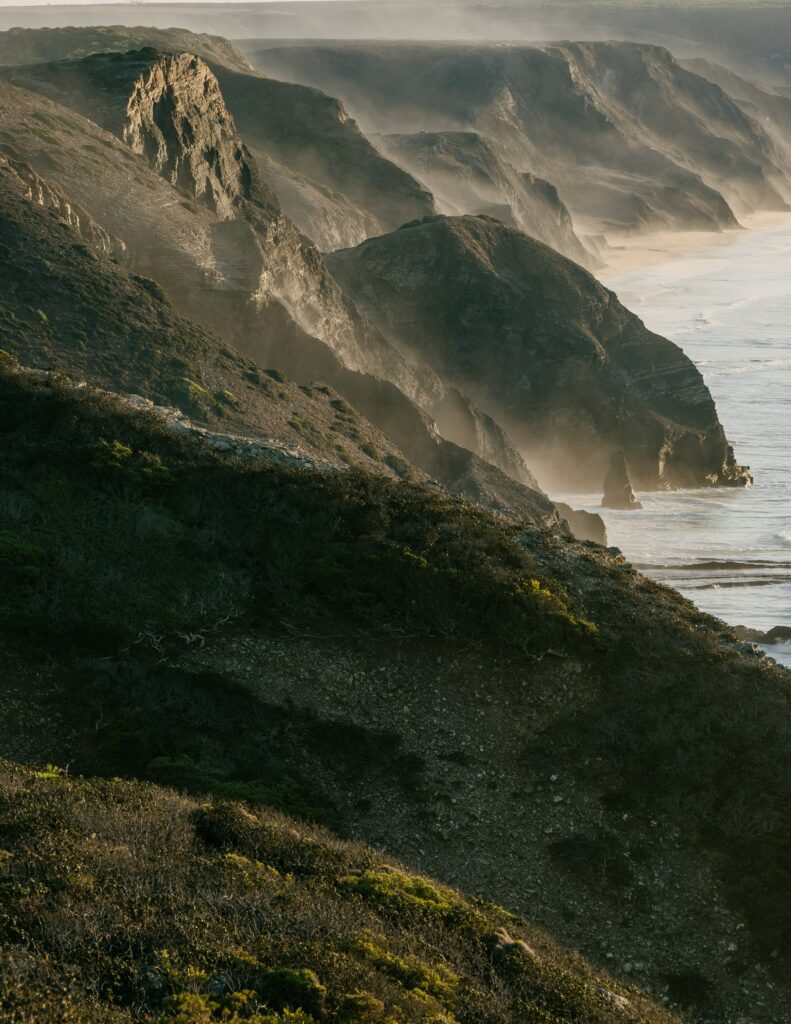 Dramatic coastal cliffs with rugged rocks and foggy sea under warm sunlight serene landscape Wallpaper