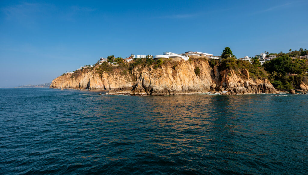 Vibrant coastal landscape with rocky cliffs lush green trees deep blue sea and clear sky wallpaper