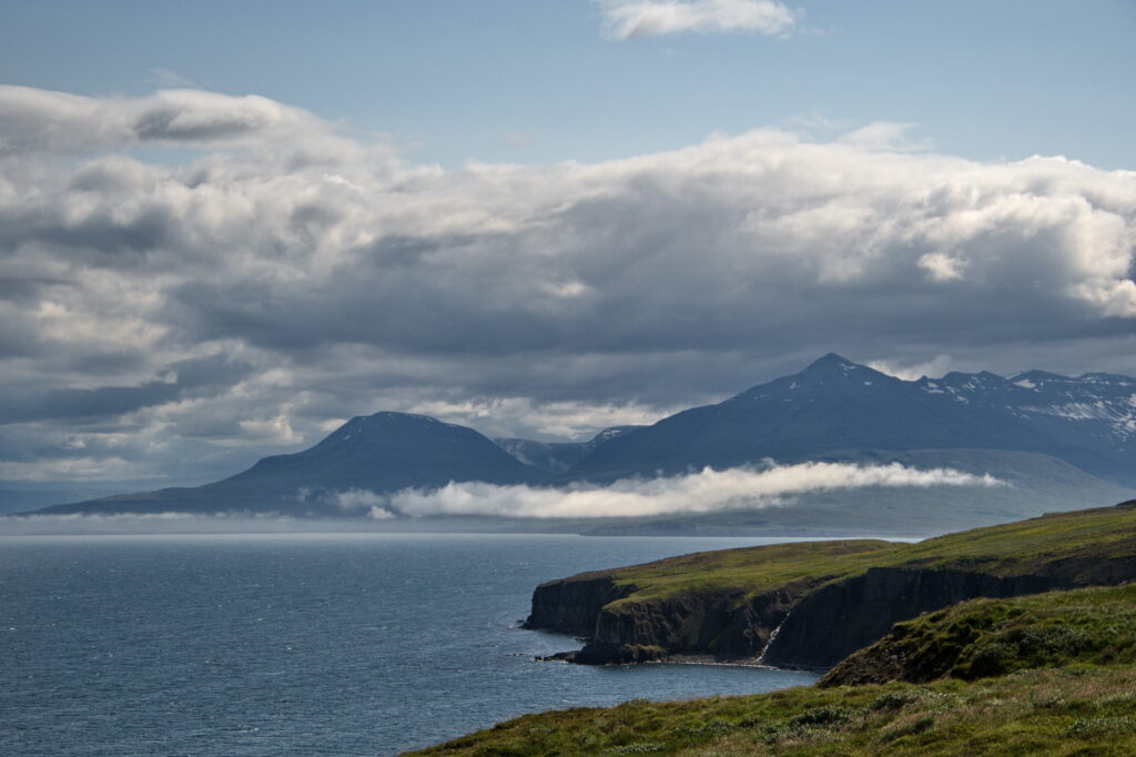 Dramatic coastal landscape with rugged mountains cliffs calm blue sea and soft drifting clouds Wallpaper