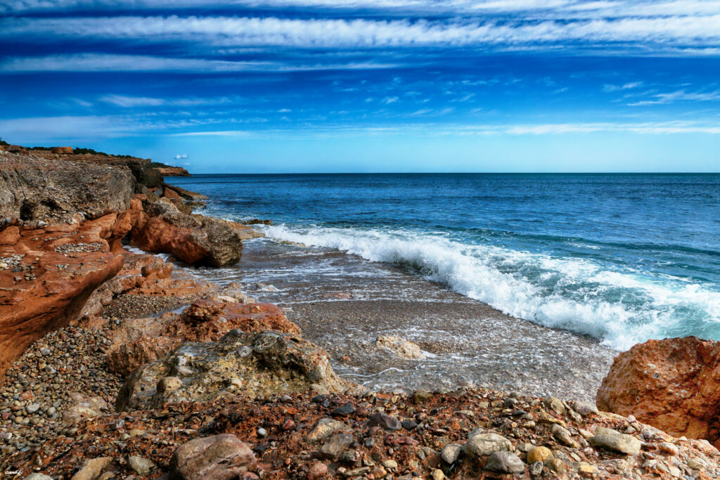 Serene coastal wallpaper with rugged rocks gentle waves and vibrant blue sky with wispy clouds