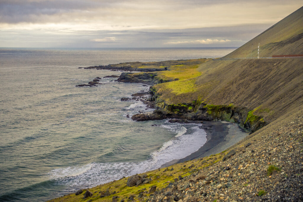 Serene coastal landscape with gentle waves rugged rocks grassy slope and moody sky wallpaper background
