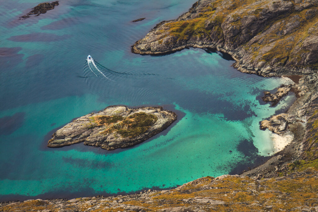 Small boat sails turquoise waters near rocky islands and cliffs in tranquil coastal landscape wallpaper