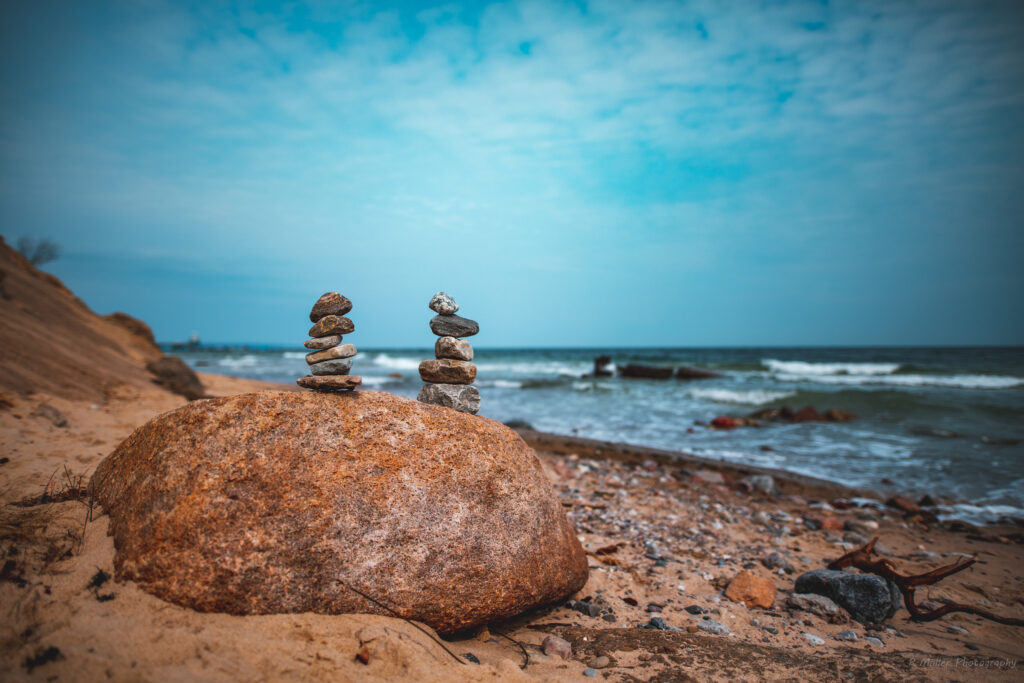Serene coastal landscape with stacked stones sandy pebble beach gentle waves under blue sky Wallpaper