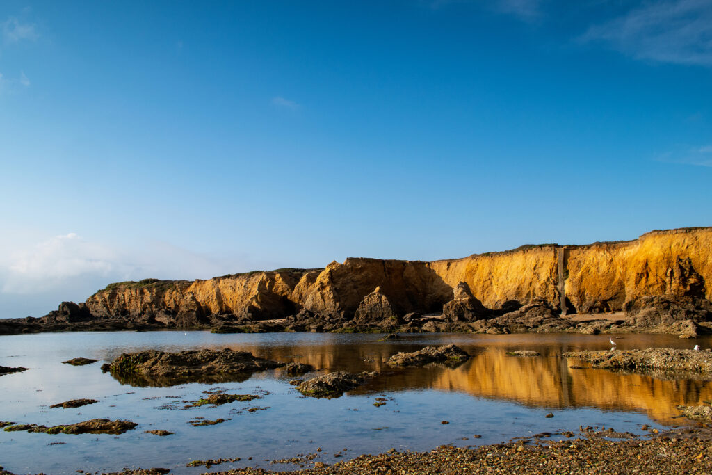Breathtaking coastal landscape with golden cliffs rocks tide pools and vibrant blue sky wallpaper background