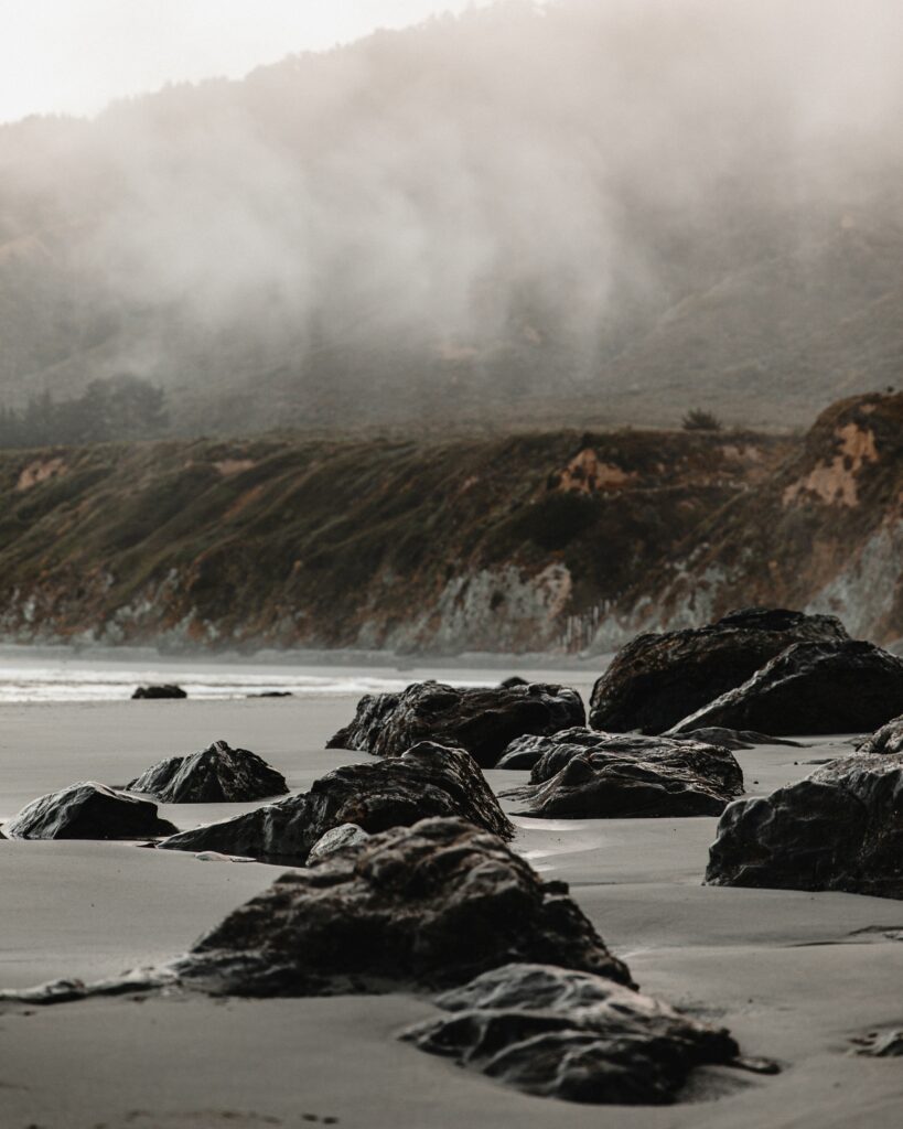 Serene coastal landscape with rugged rocks sandy shore misty cliffs earthy natural colors wallpaper