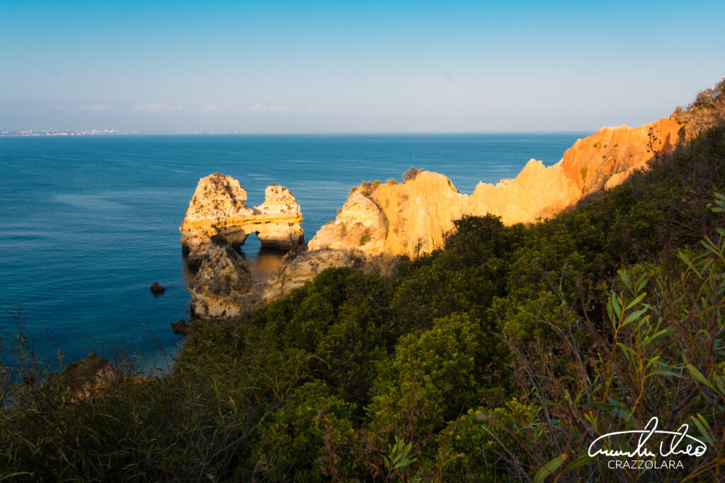 Serene coastal wallpaper with rugged rocks lush greenery golden cliffs and deep blue sea horizon