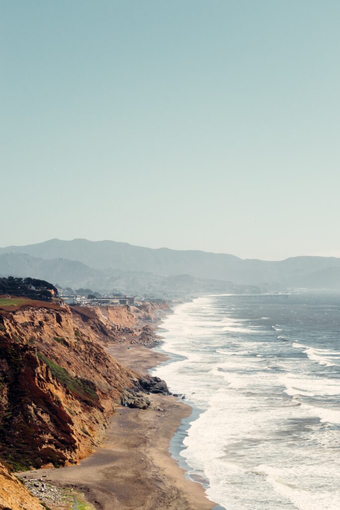 Serene coastline with rugged rocks sandy beaches cliffs calm sea gentle waves foggy mountains clear sky wallpaper