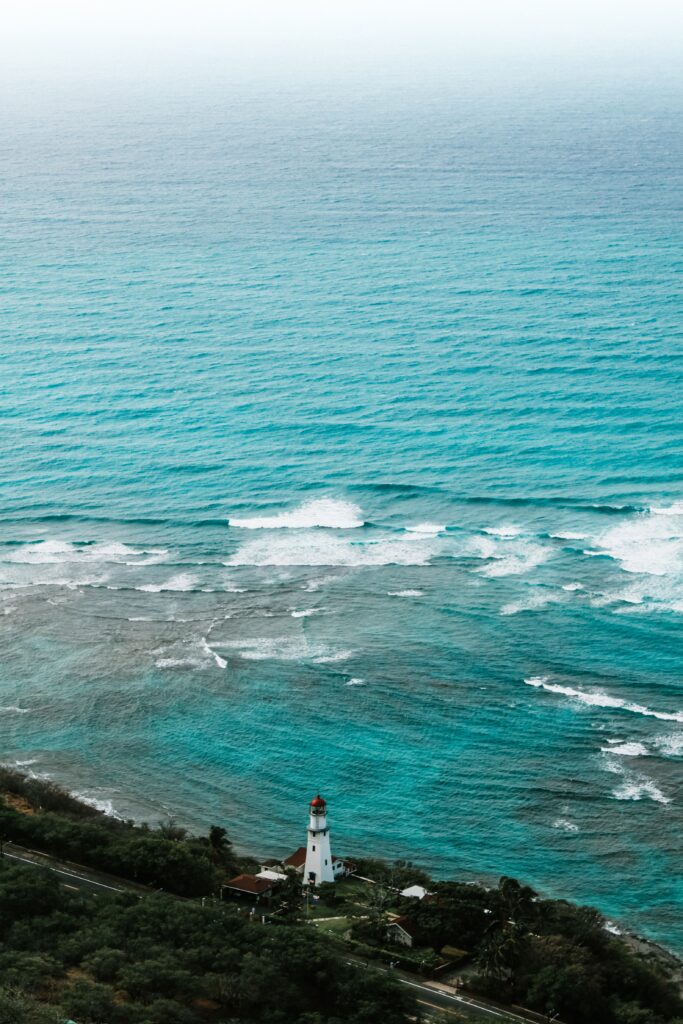 Serene coastal wallpaper with classic white lighthouse lush greenery and turquoise ocean waves