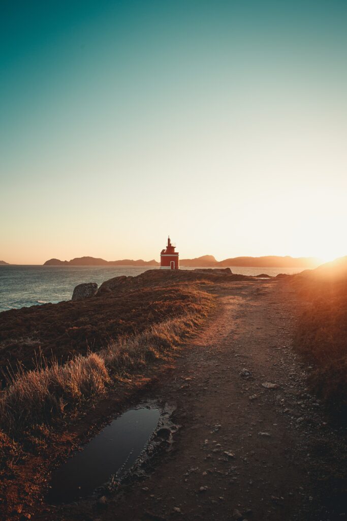 Serene coastal lighthouse on rugged rocks at sunset with winding road and natural grasses wallpaper