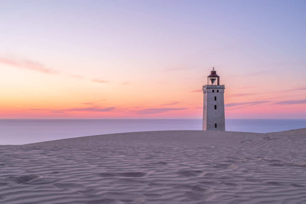 Solitary lighthouse on rippled sands at sunset with pastel pink lavender sky over calm sea Wallpaper