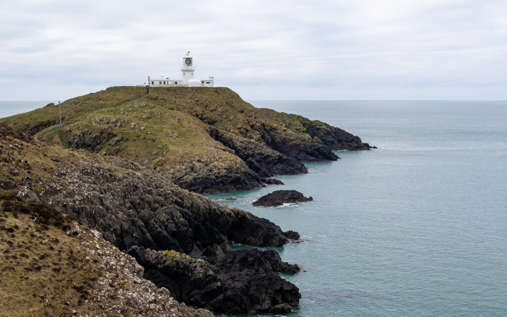 Serene coastal wallpaper with white lighthouse on cliffs overlooking calm blue sea and grassy slopes