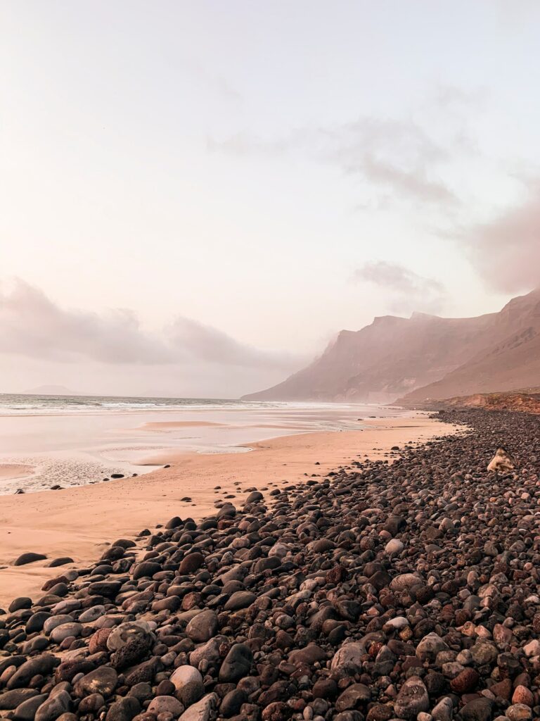 Serene coastal wallpaper with smooth pebbles dark rocks sandy shore pastel sky mountains