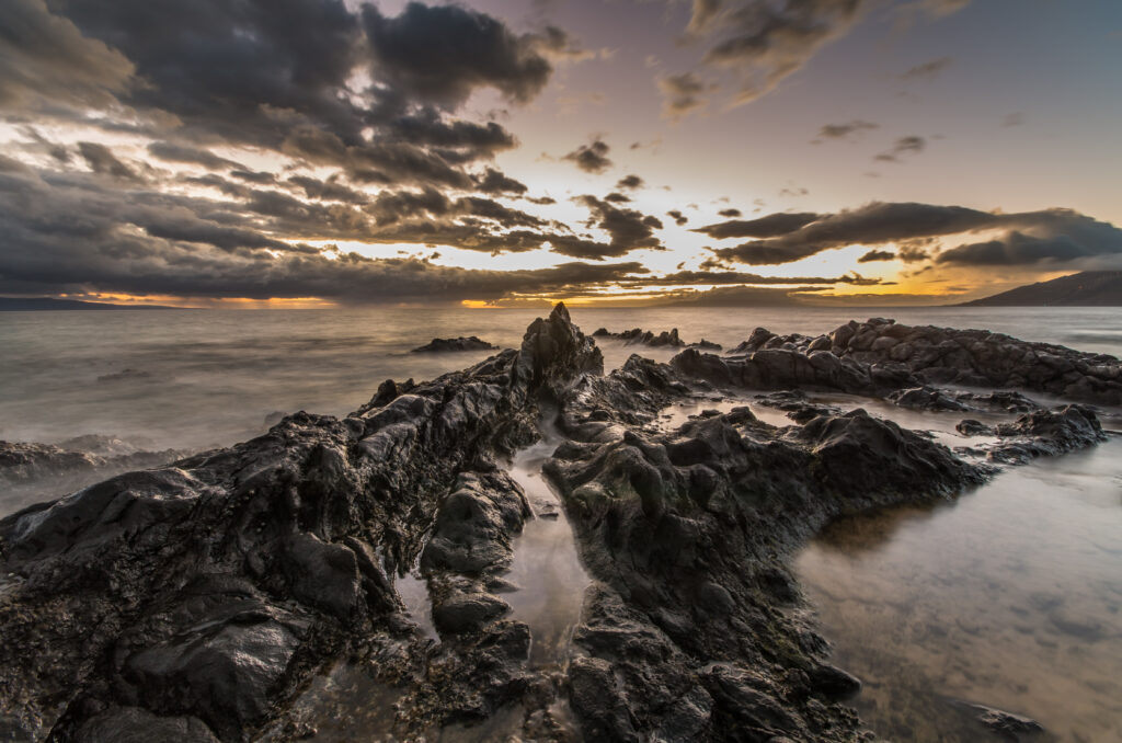 Rugged coastal rocks and calm water under dramatic sky with warm sunlight reflections wallpaper