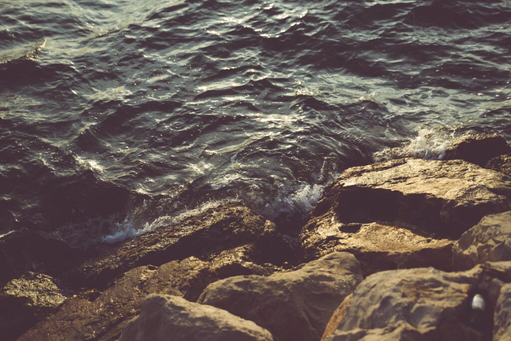 Rugged coastal stones with gentle sea waves in warm natural light serene shoreline wallpaper