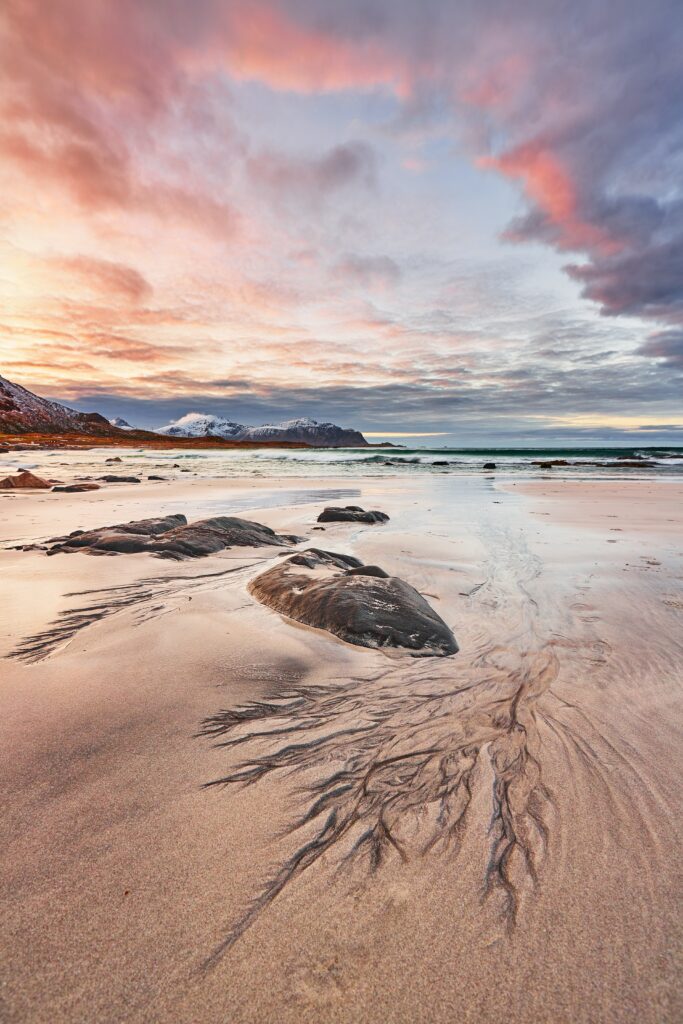 Serene coastal wallpaper with soft sand patterns smooth rocks and tranquil shoreline under colorful sky