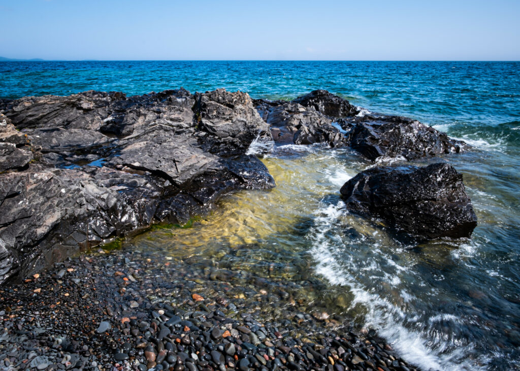 Serene coastal wallpaper with rugged stones smooth pebbles turquoise sea and clear blue sky
