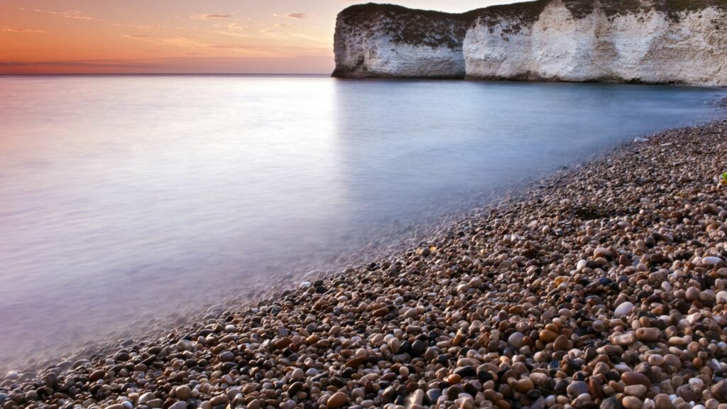 Serene coastal scene with smooth stones white cliffs pastel sunset waves lapping shore wallpaper