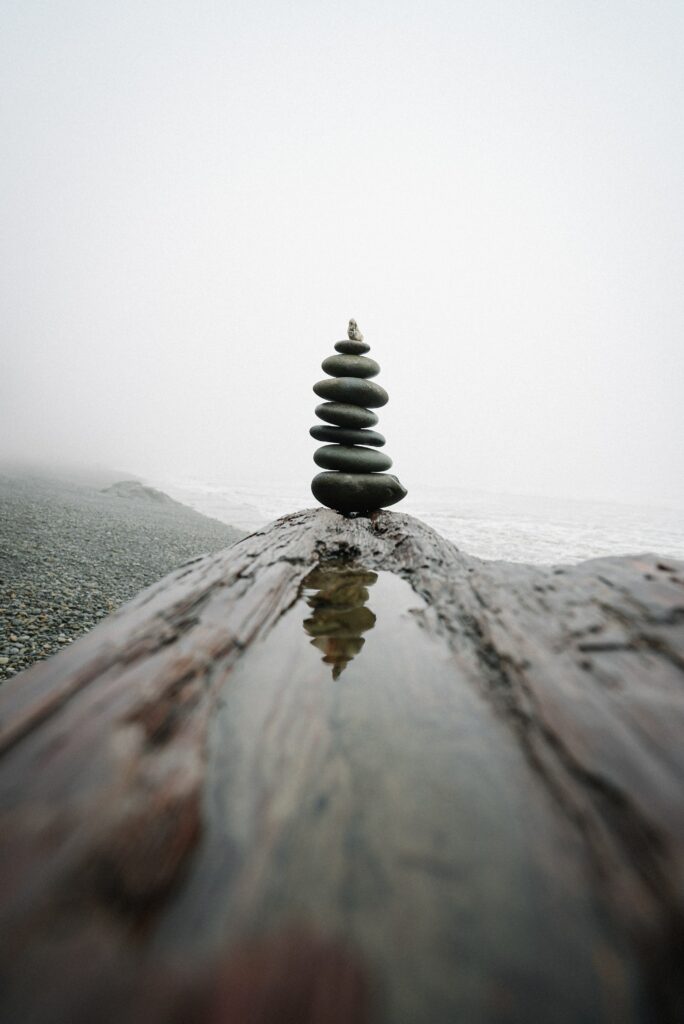 Serene coastal wallpaper with balanced dark stones on weathered log and misty soft light