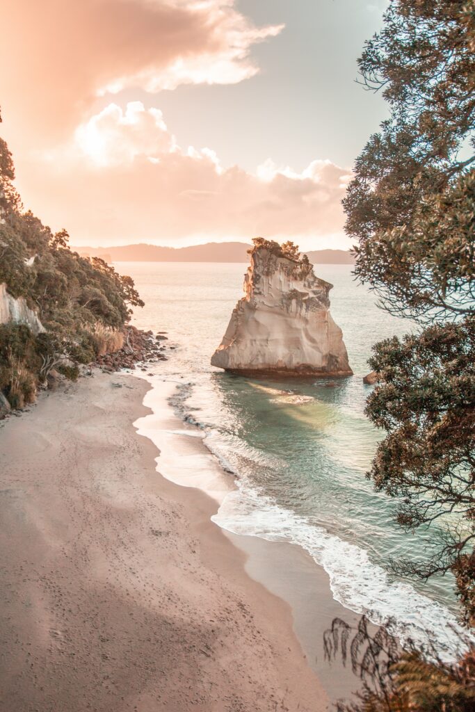 Serene coastal landscape with sandy beach rugged rocks pastel sunrise sky and gentle waves Wallpaper