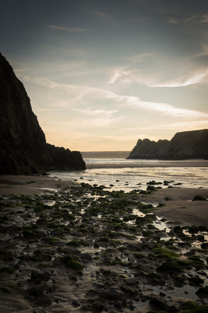 Serene coastal sunset with rugged rocks waves and cliffs in earthy muted tones wallpaper background