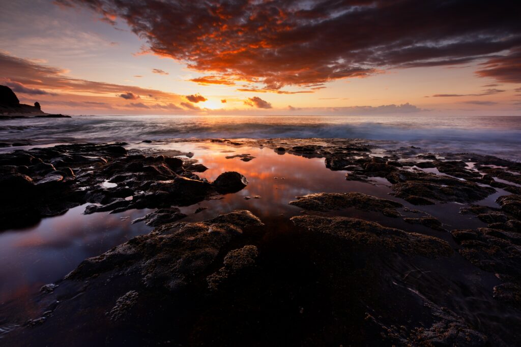 Sunset seascape with smooth stones and jagged rocks reflecting vibrant sky in tide pools Wallpaper