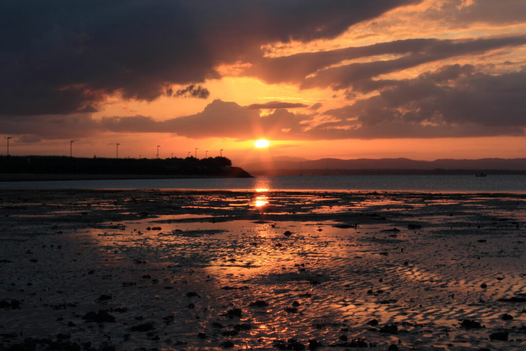 Serene coastal sunset wallpaper with golden sun dipping below horizon and warm colorful sky