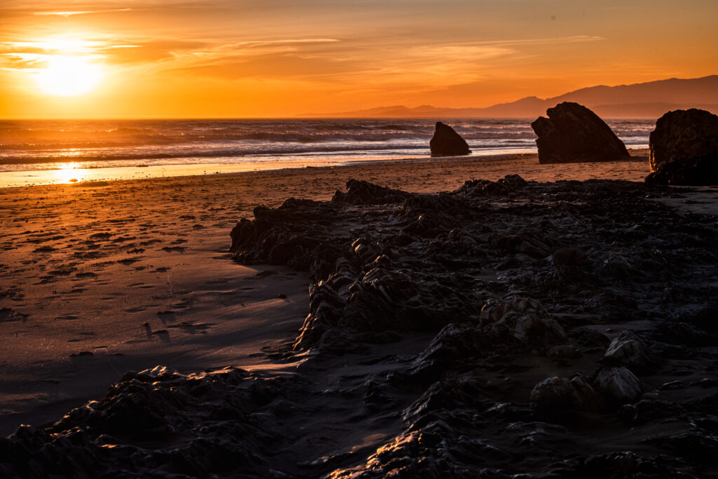 Sunset coastal wallpaper with gentle waves sandy shores and rugged rocks in warm golden hues