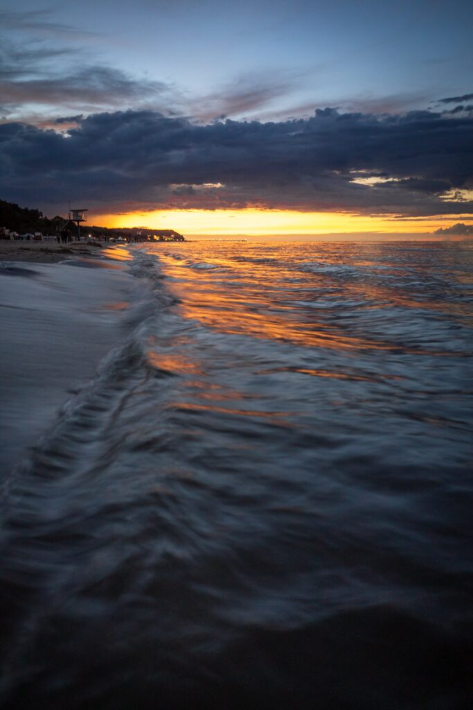 Sunset coastal scene with golden sea waves and dramatic clouds creating tranquil beach wallpaper