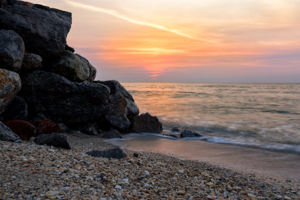 Serene coastal sunset wallpaper with rugged rocks calm sea waves and pastel sky hues